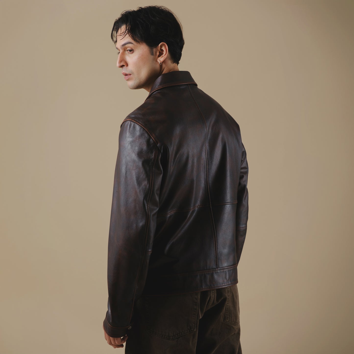 Man wearing a dark leather jacket against a beige background
