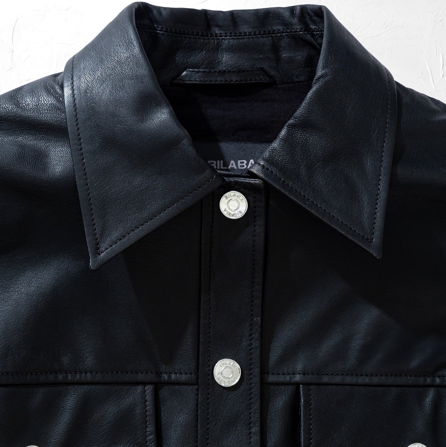 Close-up of a black trucker leather jacket with a brand label on a white background