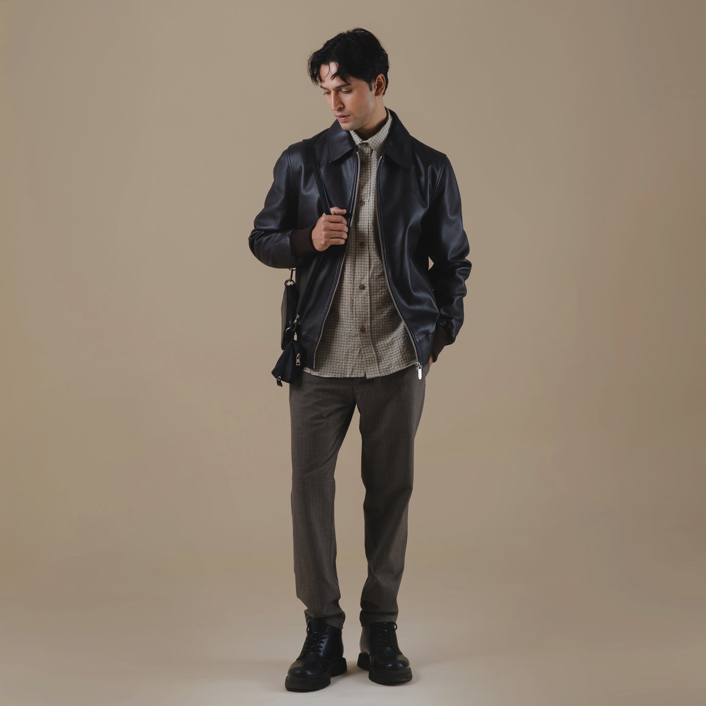 Man wearing a brown leather jacket and dark pants against a beige background