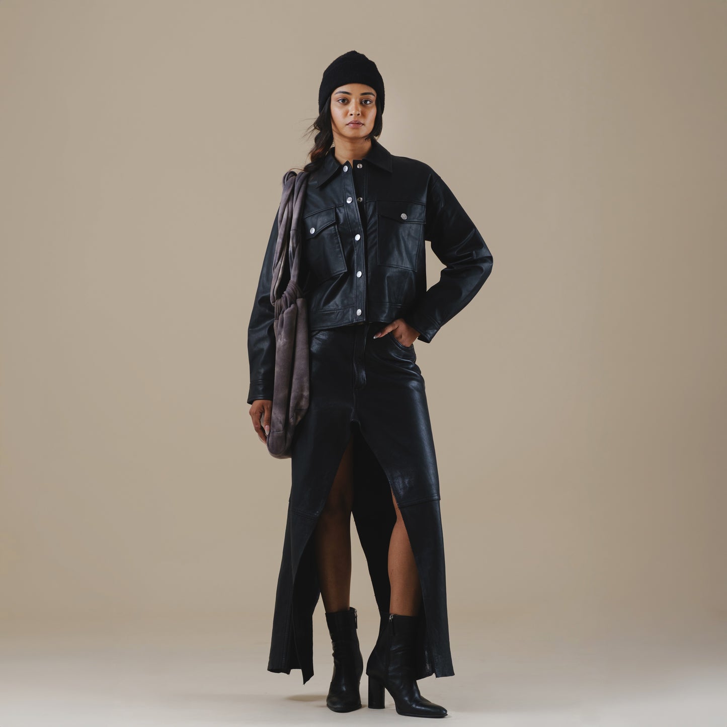 Person wearing a black trucker jacket, leather pants, and boots on a beige background