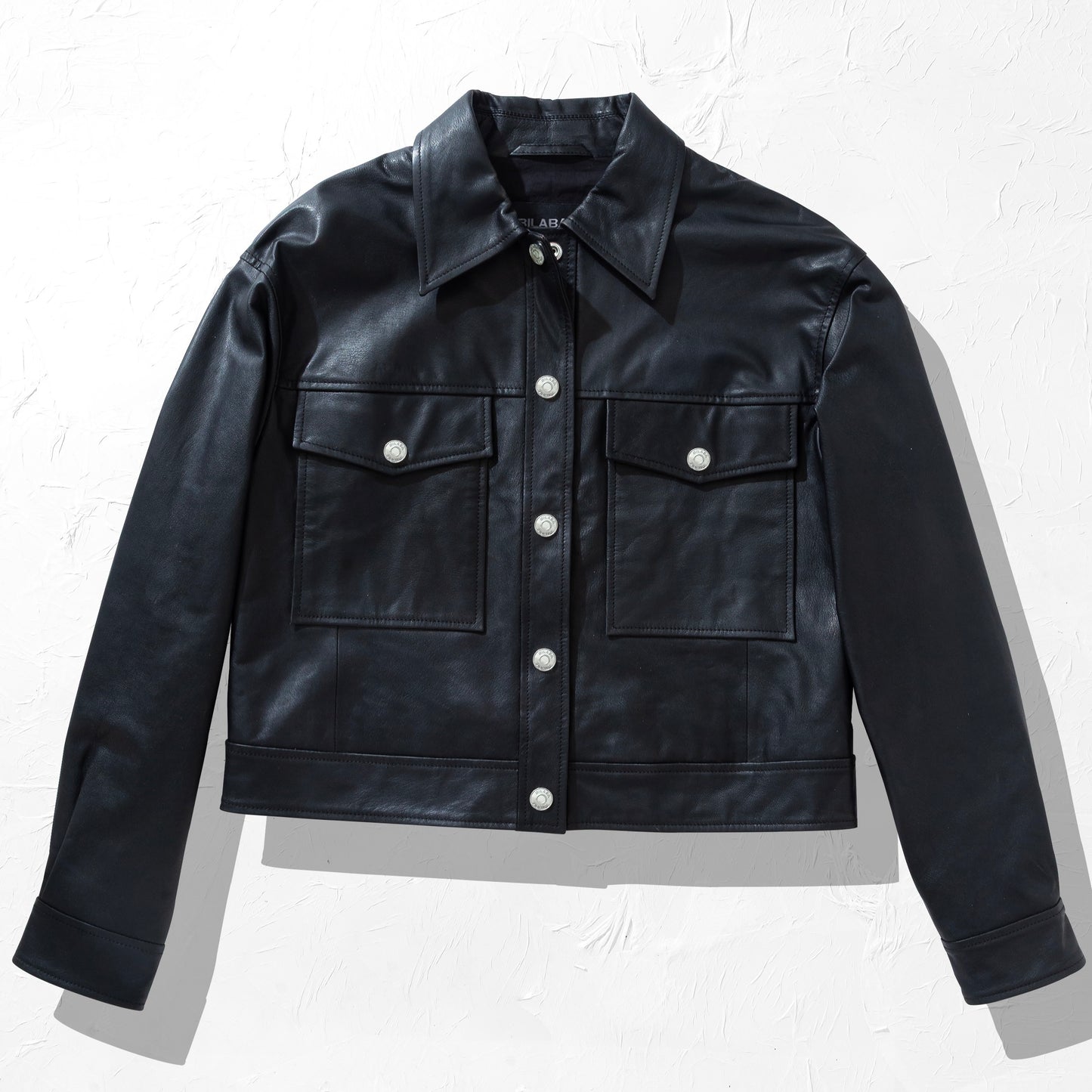 Black trucker leather jacket with white buttons on a light gray background