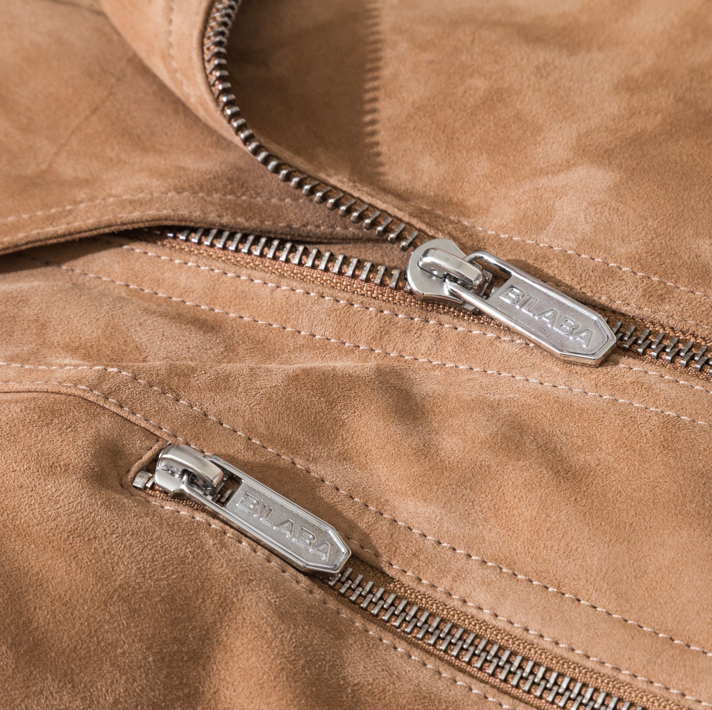 Close-up of a beige suede jacket with silver zippers