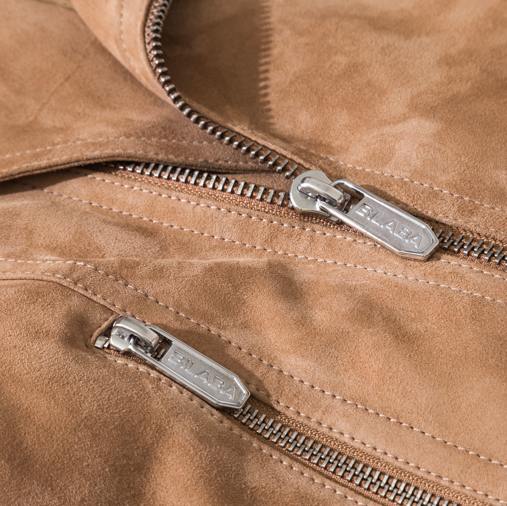 Close-up of a beige suede jacket with silver zippers