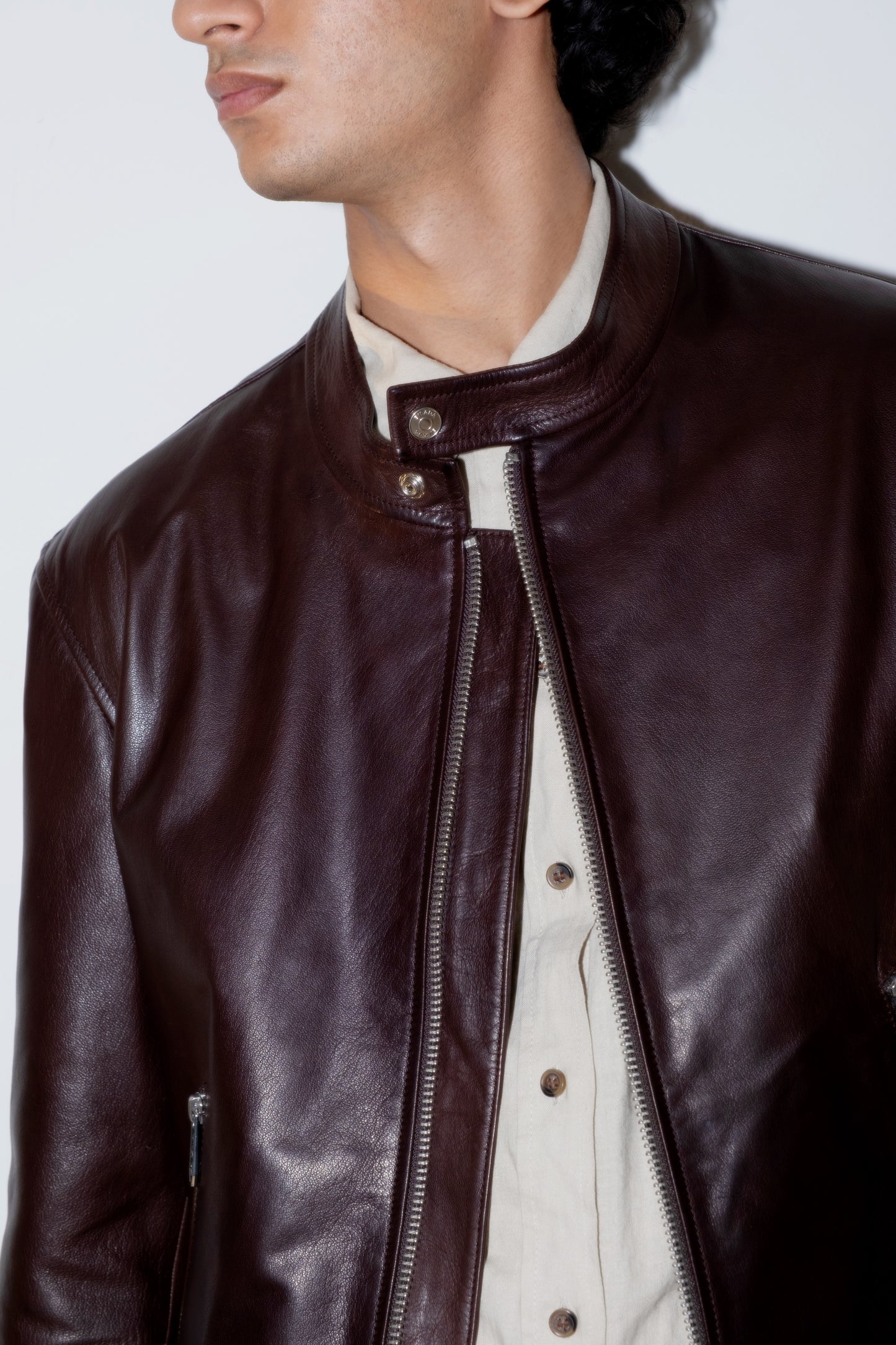 Close-up of a person wearing a dark brown leather jacket with a white shirt underneath.