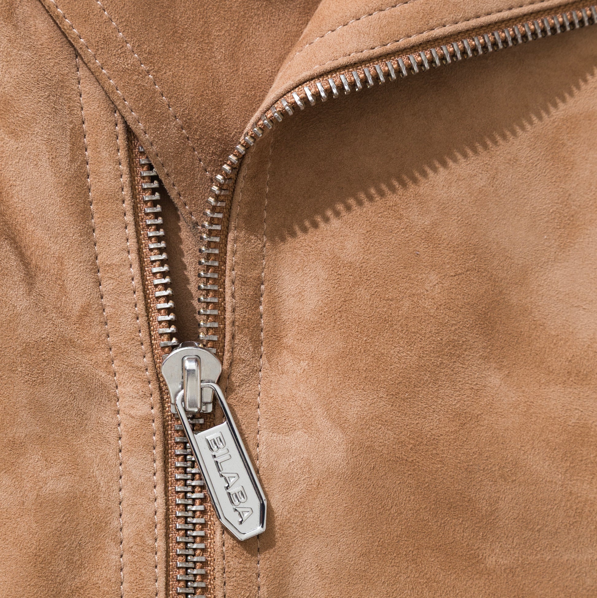 Close-up of a brown suede jacket with a zipper, featuring the brand 'BILABA'.