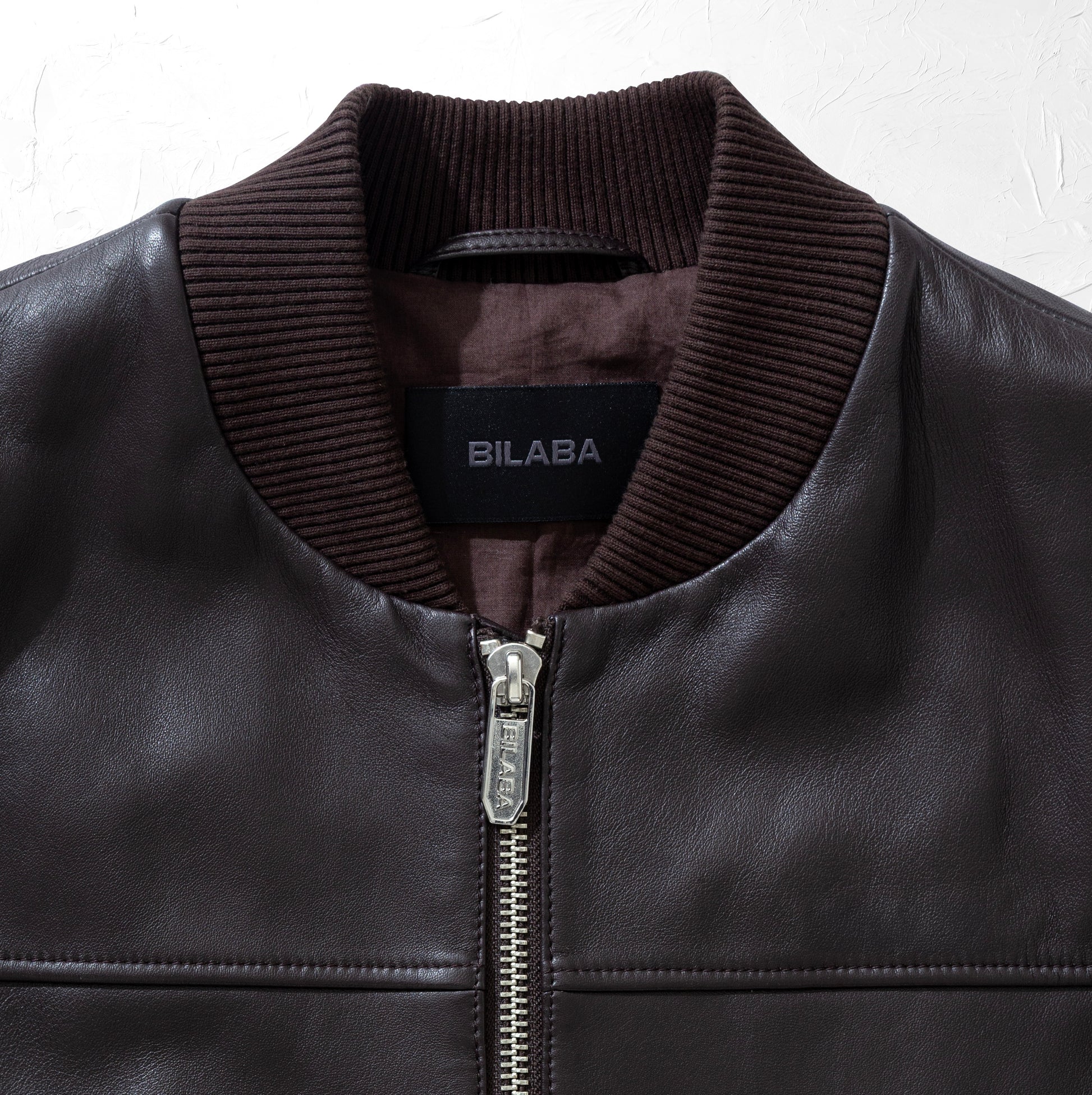 Close-up of a brown bomber leather jacket with a visible brand label 'BILABA' on a white background
