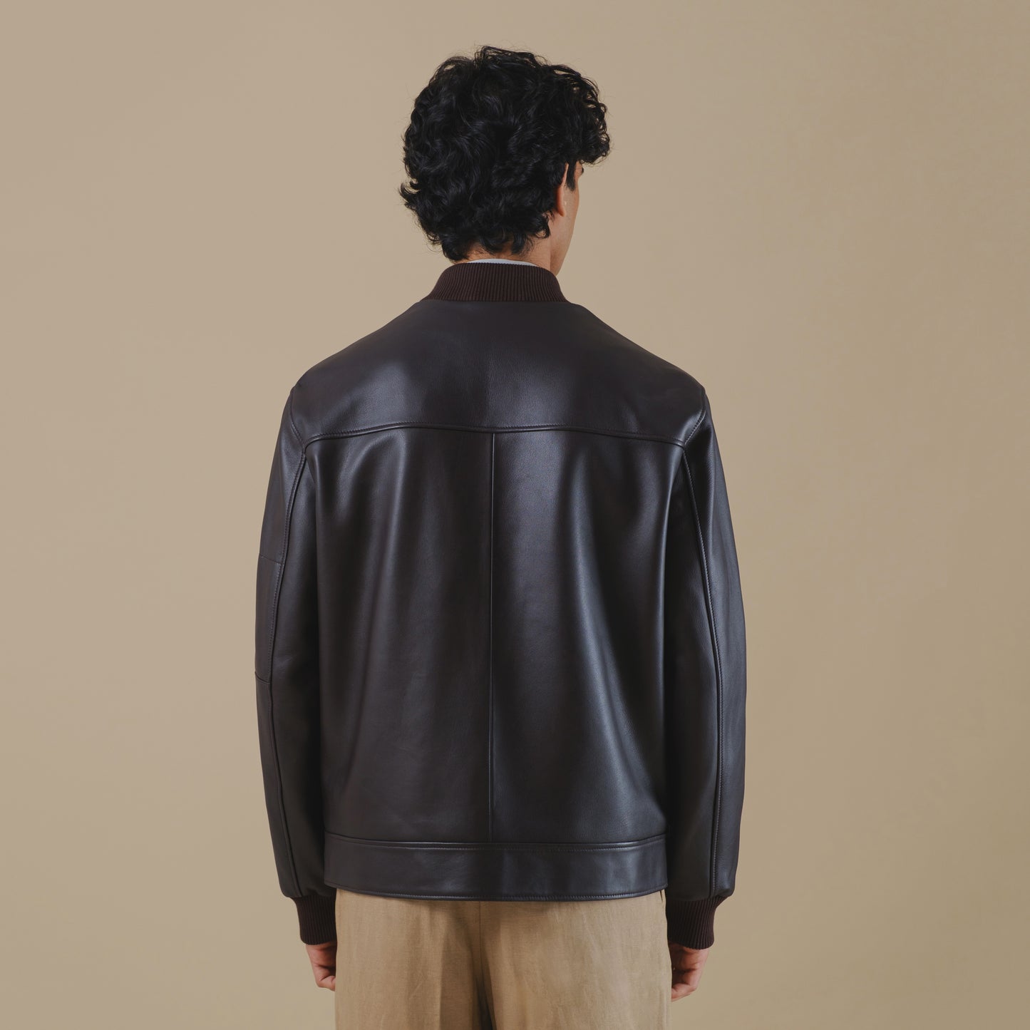 Person wearing a brown bomber leather jacket on a beige background
