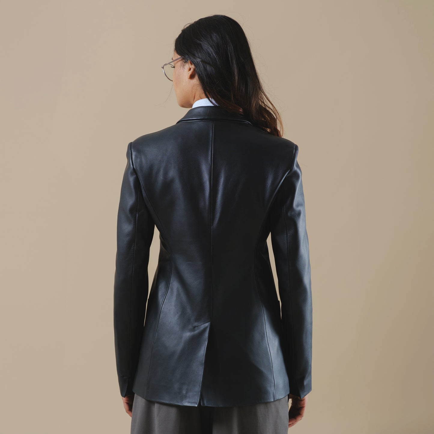 Person wearing a black leather blazer jacket on a beige background