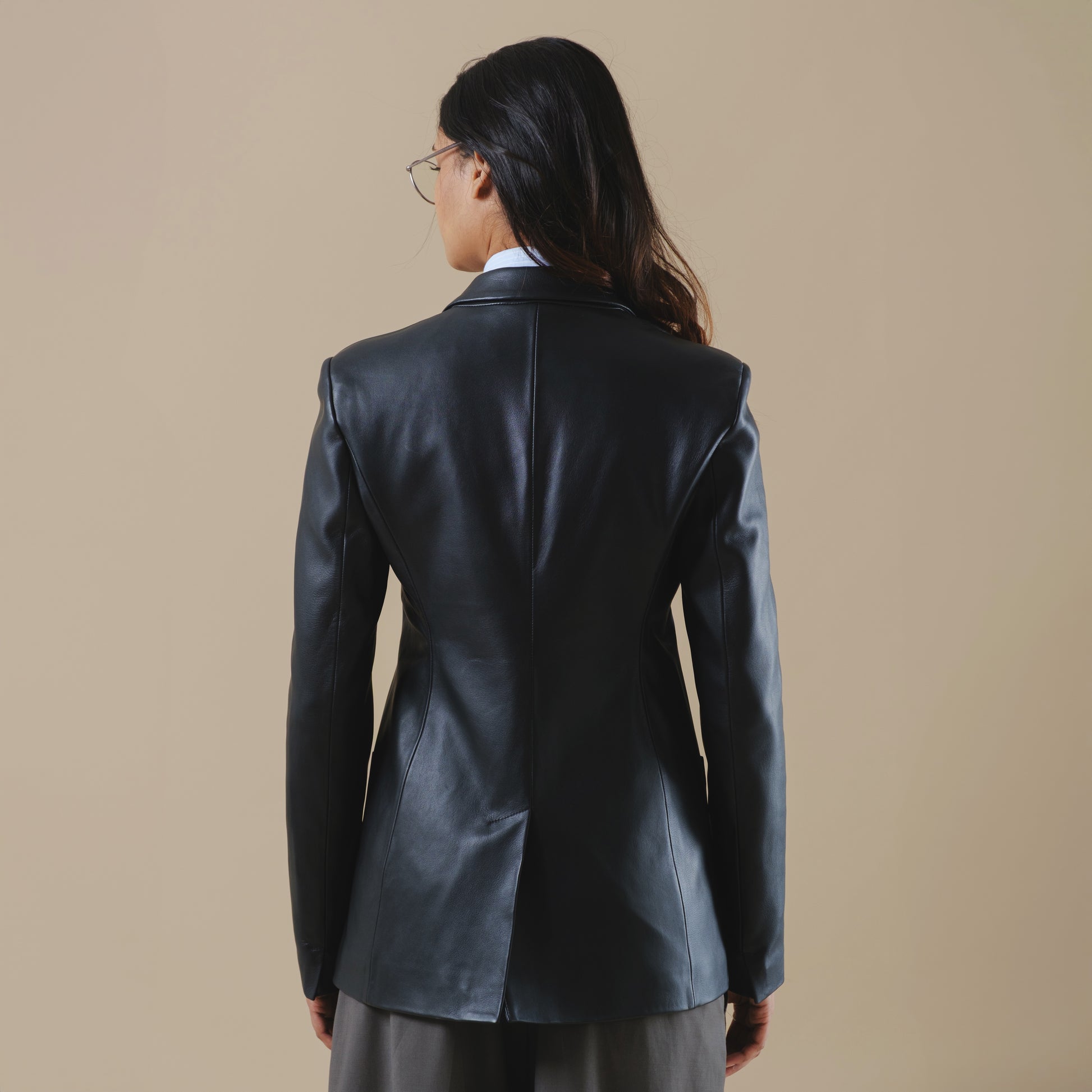 Person wearing a black leather blazer jacket on a beige background