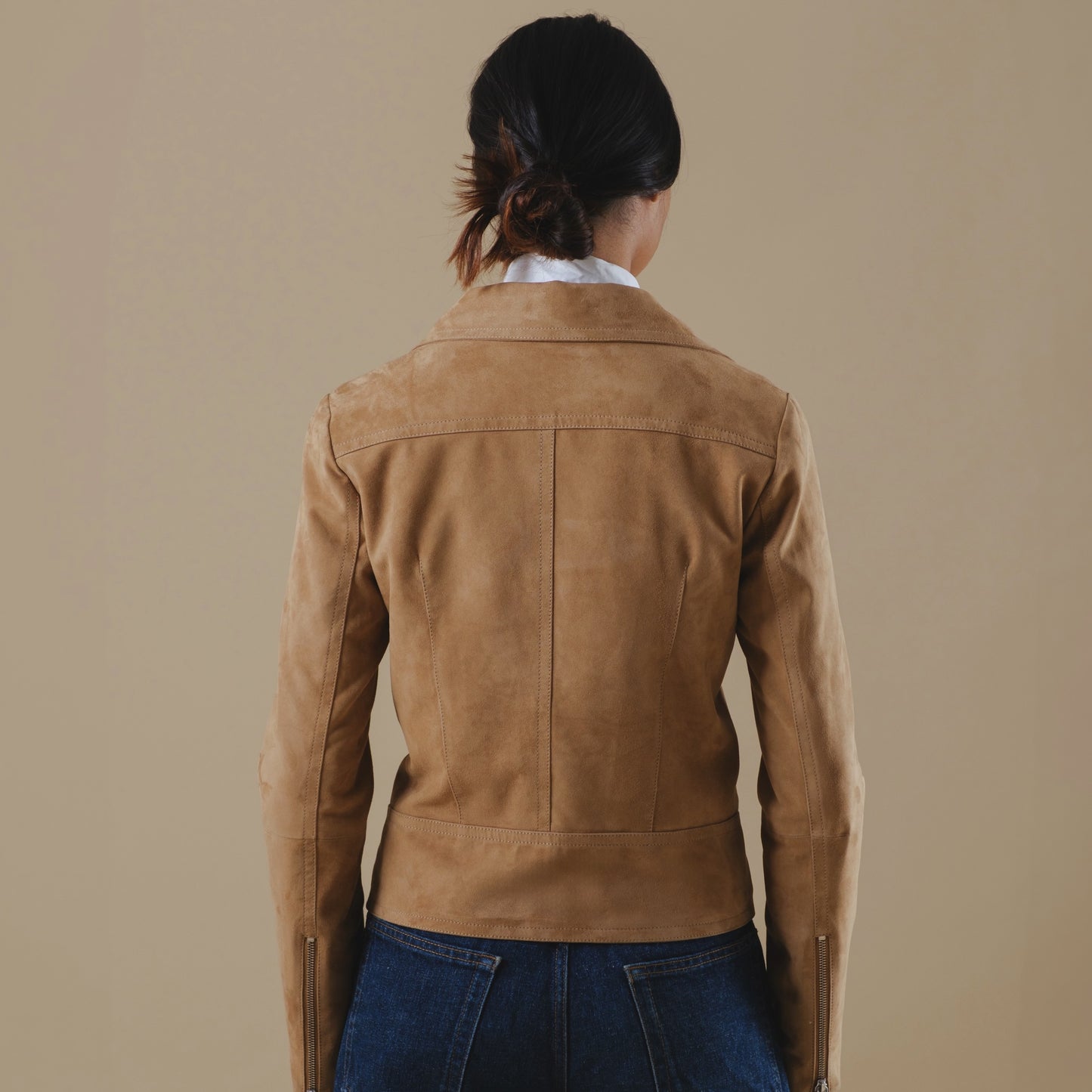 Person wearing a tan leather jacket on a beige background