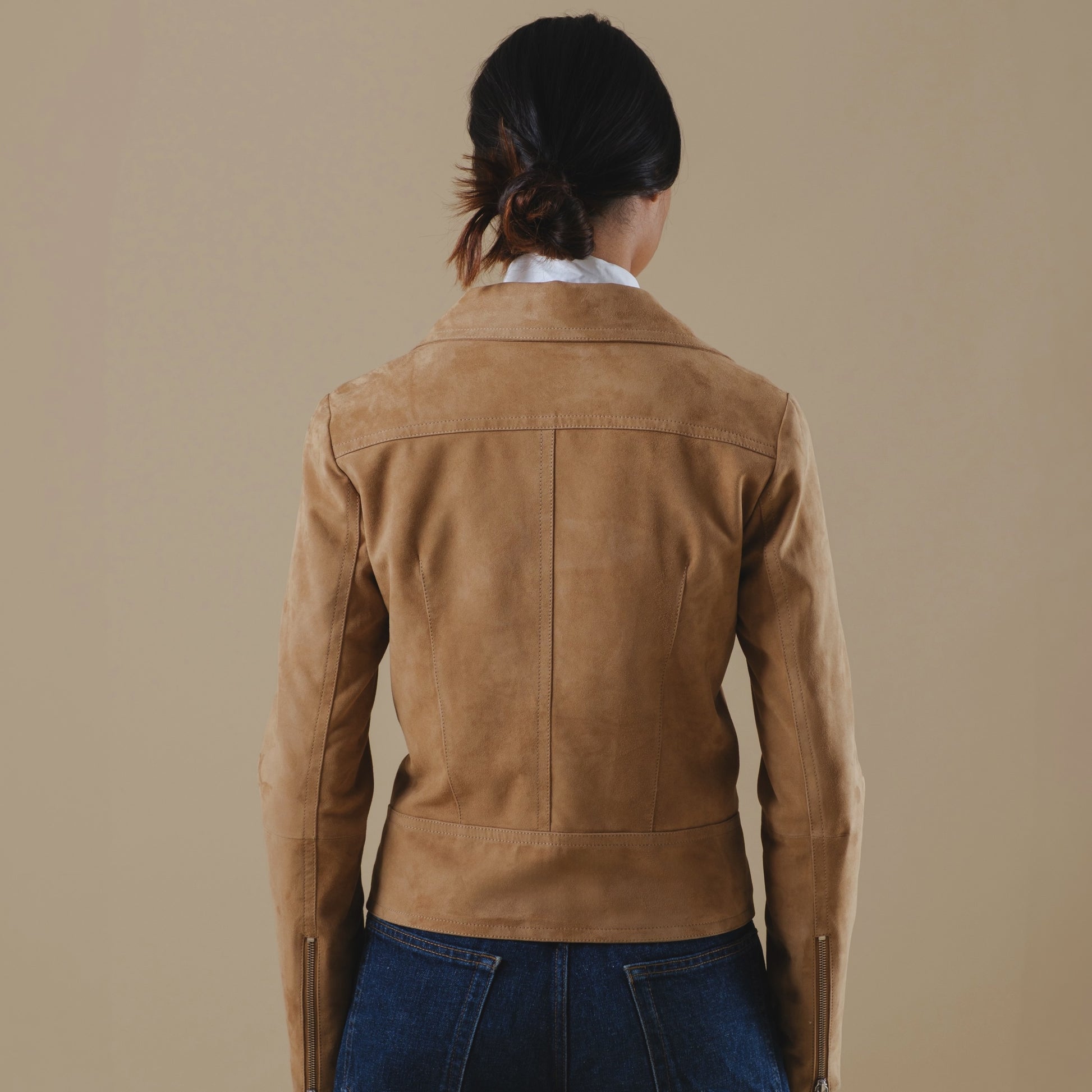 Person wearing a tan leather jacket on a beige background