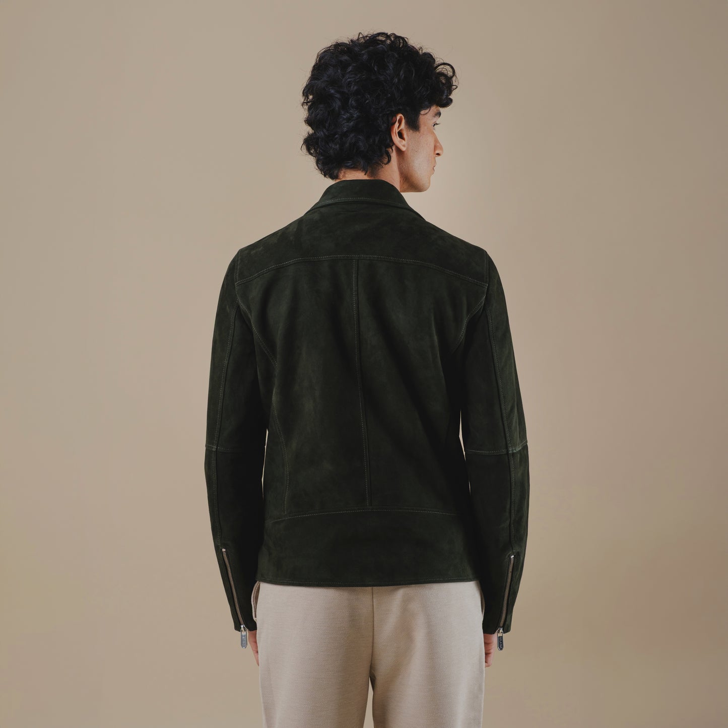 Man wearing a dark green suede jacket on a beige background