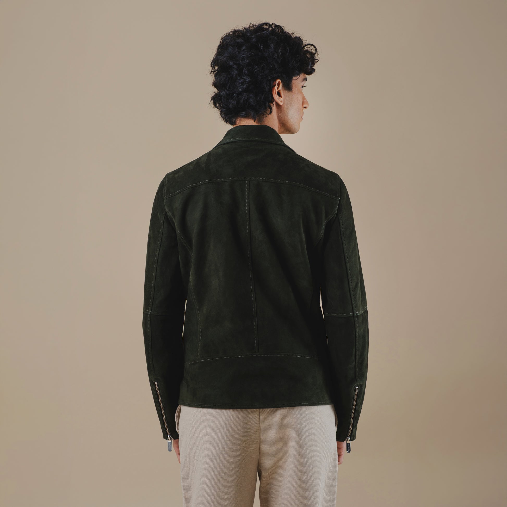 Man wearing a dark green suede jacket on a beige background