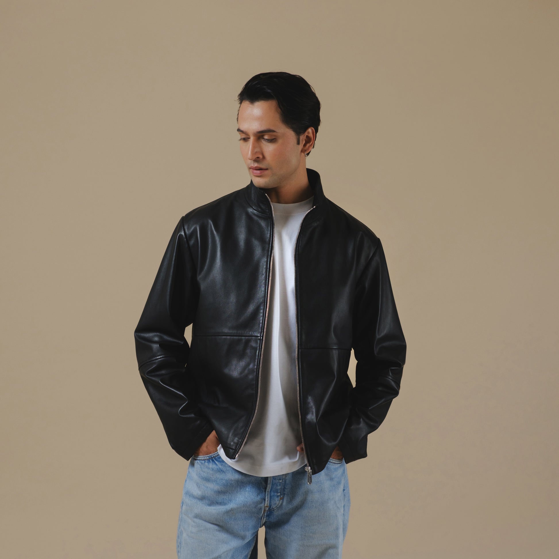 Man wearing a black leather jacket and blue jeans against a beige background