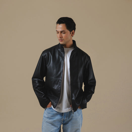 Man wearing a black leather jacket and blue jeans against a beige background