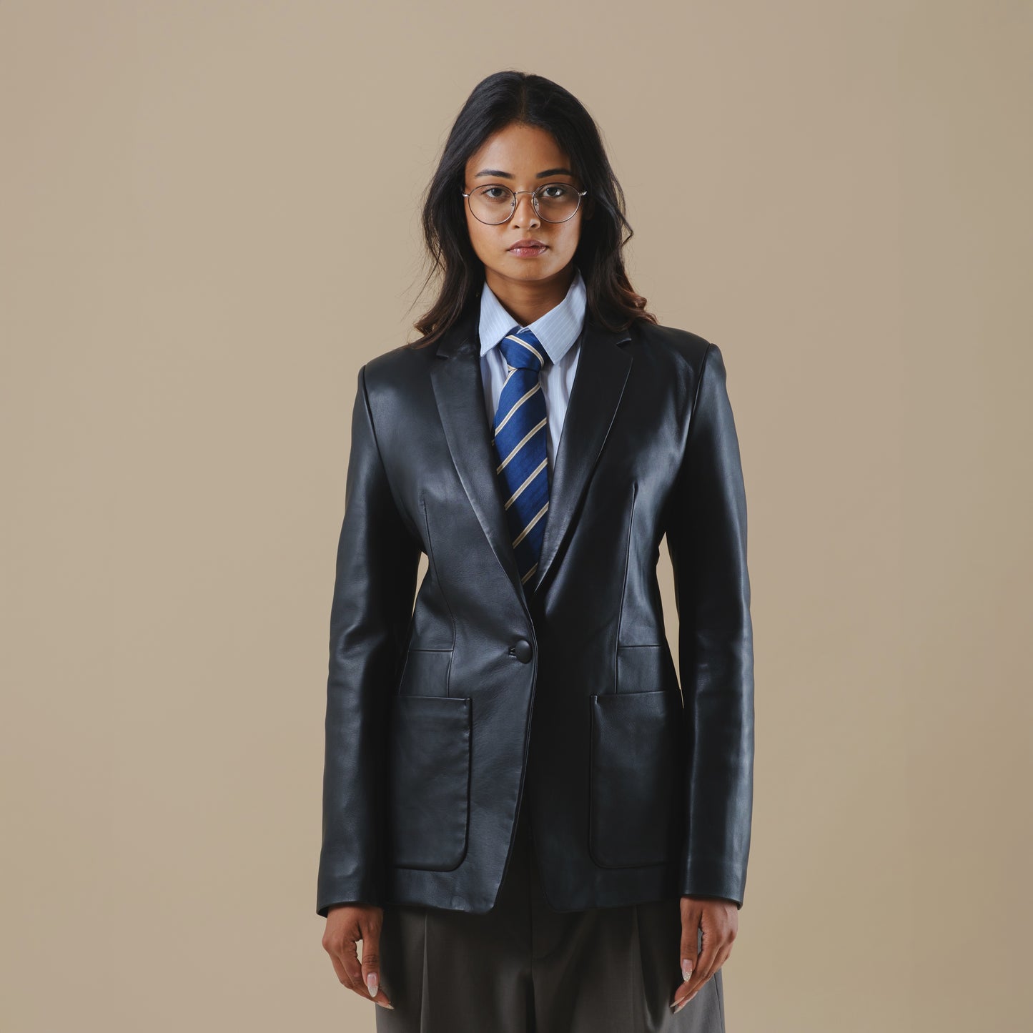 Person wearing a black leather blazer jacket and tie on a beige background