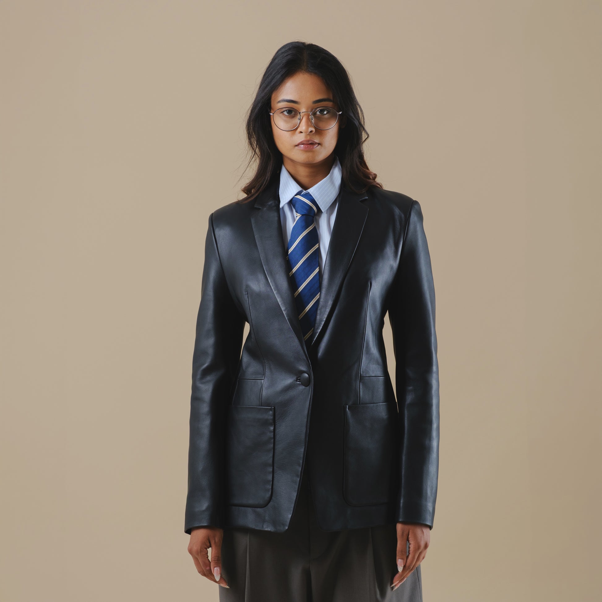 Person wearing a black leather blazer jacket and tie on a beige background