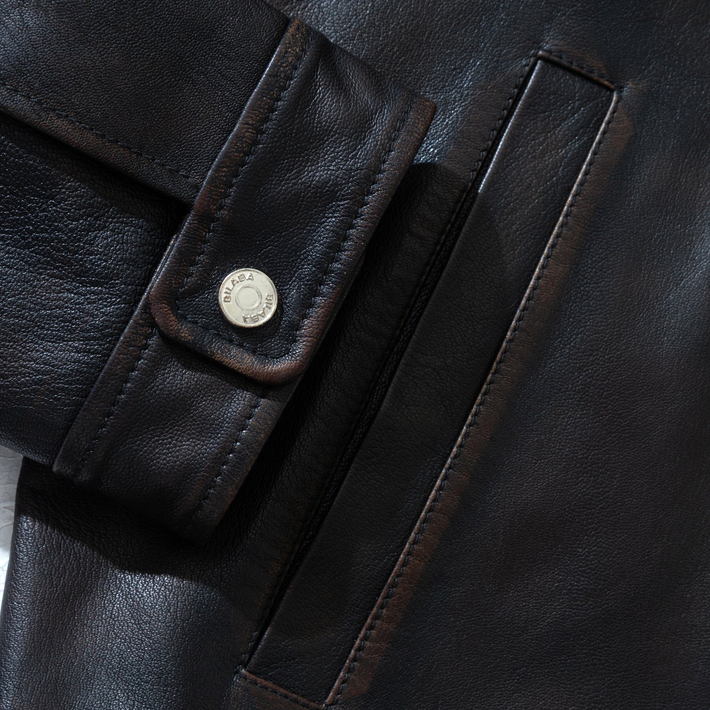 Close-up of a black vintage leather jacket with a button and brand logo.