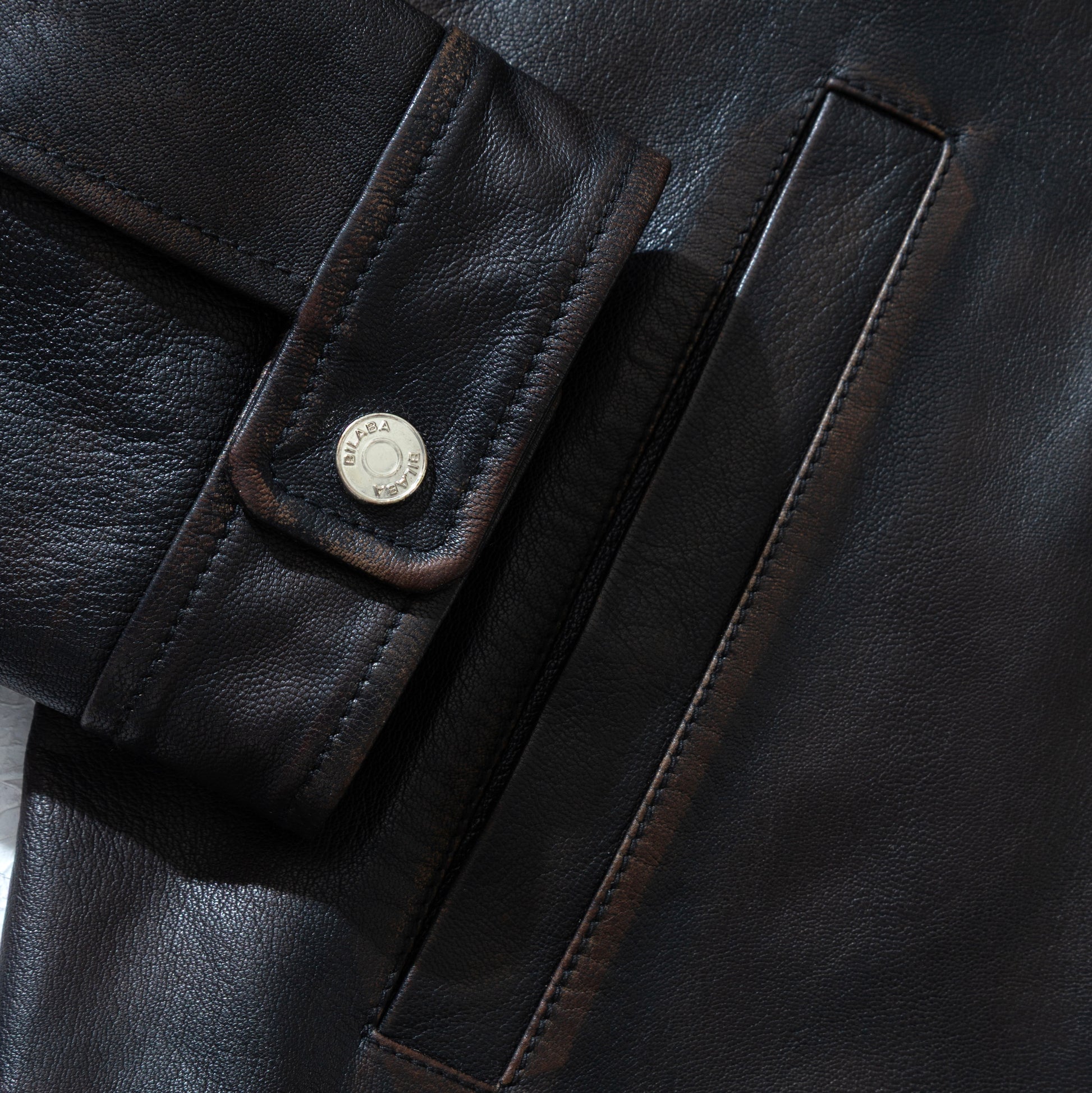 Close-up of a black vintage leather jacket with a button and brand logo.