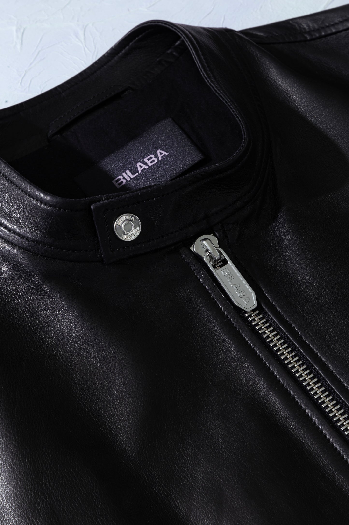 Close-up of a black leather jacket with a brand label on a light gray background