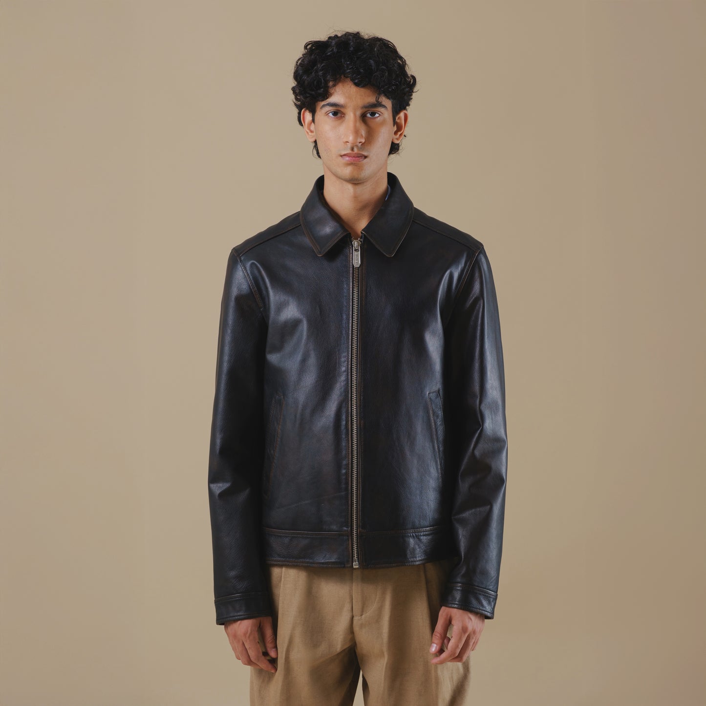 Man wearing a black vintage leather jacket against a beige background