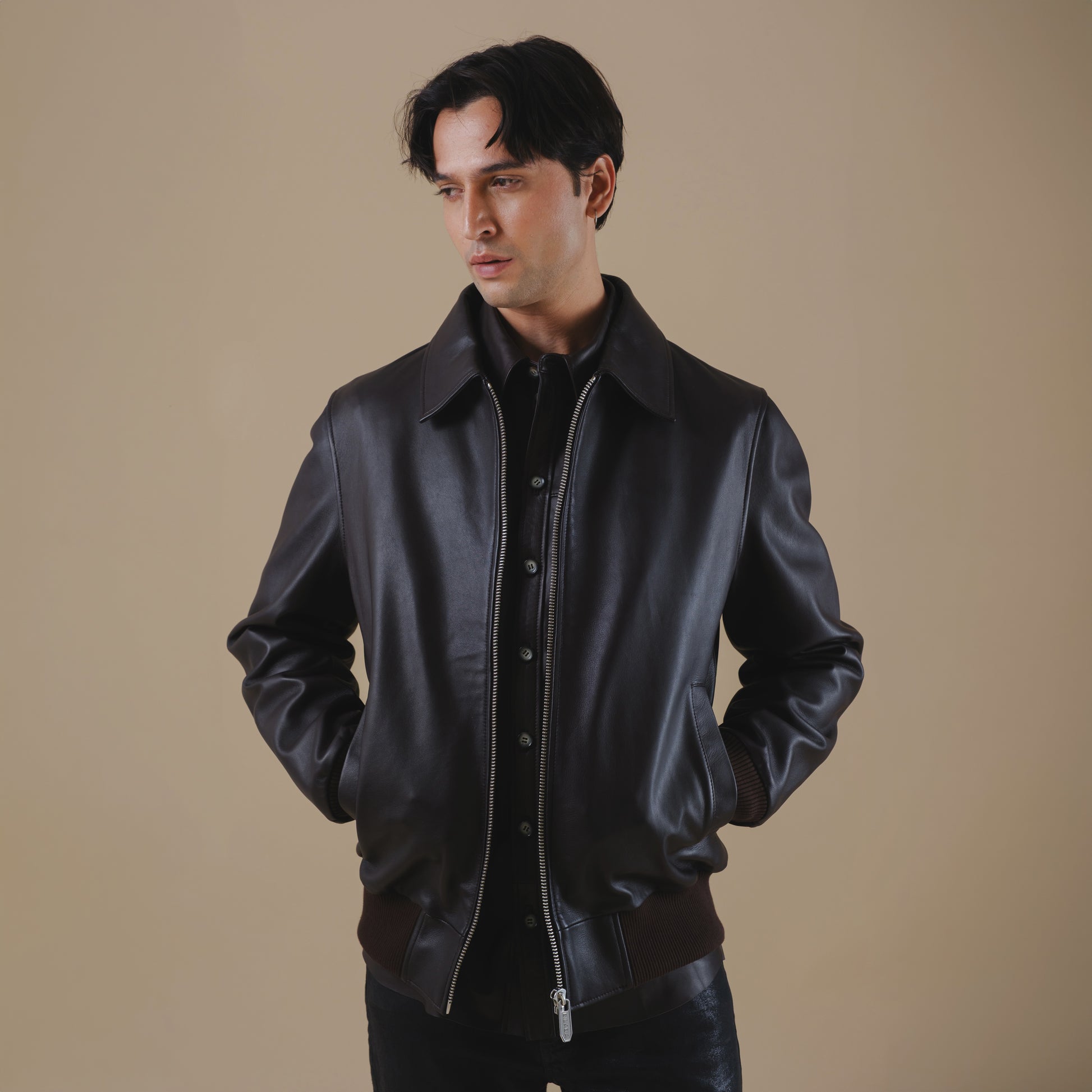 Man wearing a brown bomber leather jacket against a beige background