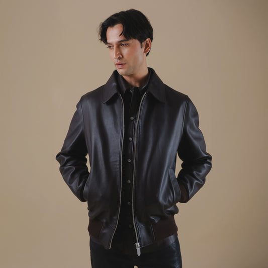 Man wearing a brown bomber leather jacket against a beige background