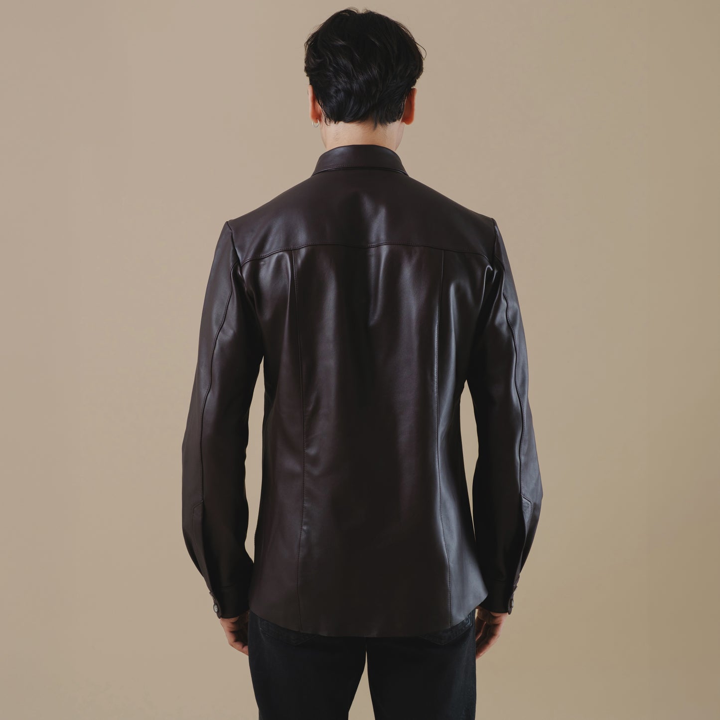 Person wearing a dark brown shirt leather on a beige background