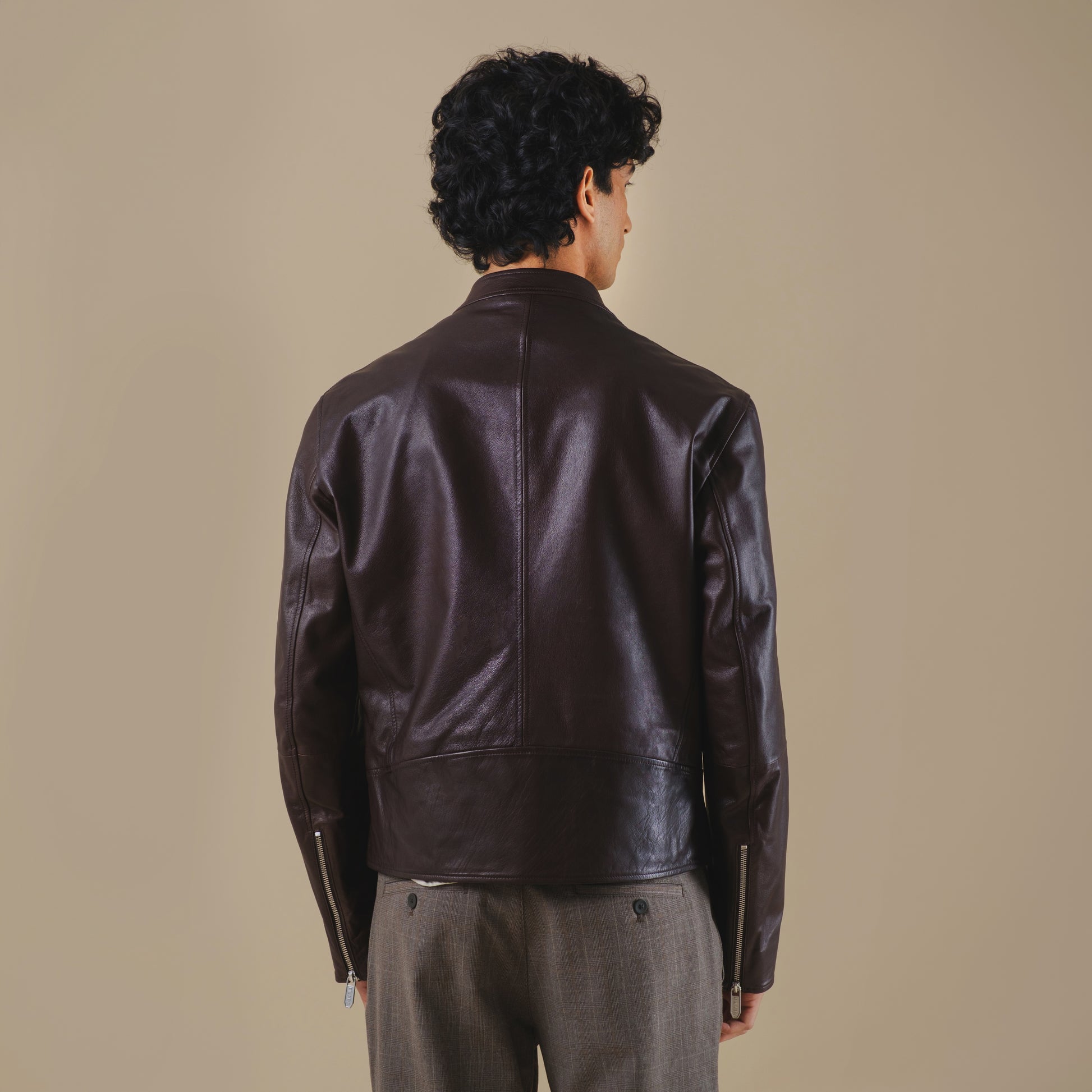 Man wearing a dark brown leather jacket against a beige background