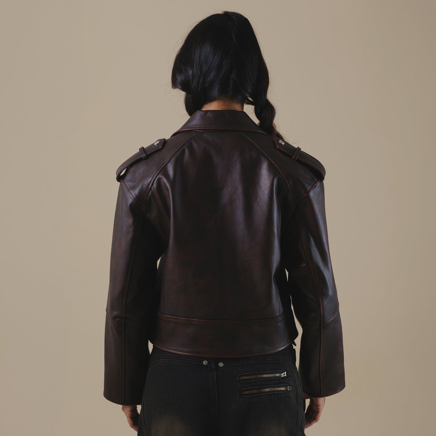 Person wearing a brown leather jacket on a beige background