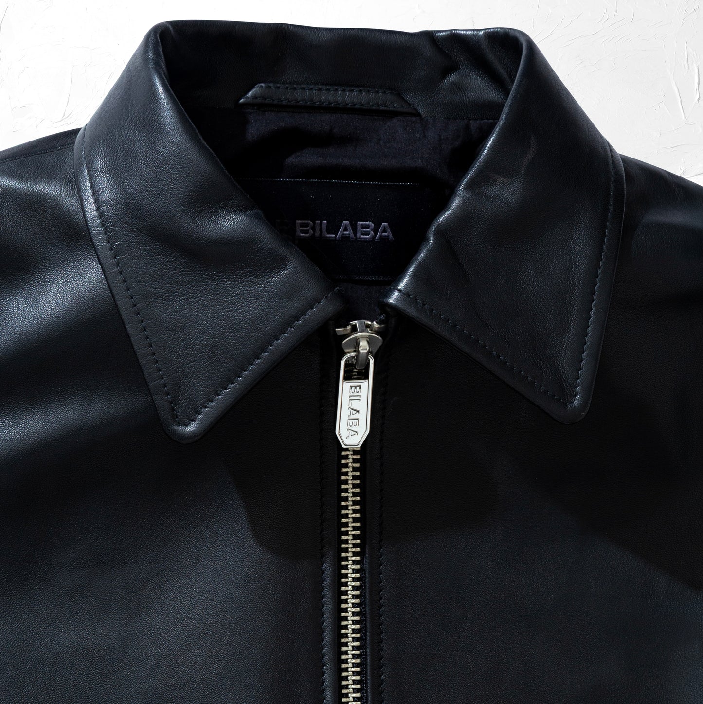 Close-up of a black leather jacket with a zipper, featuring the brand 'BILABA'.