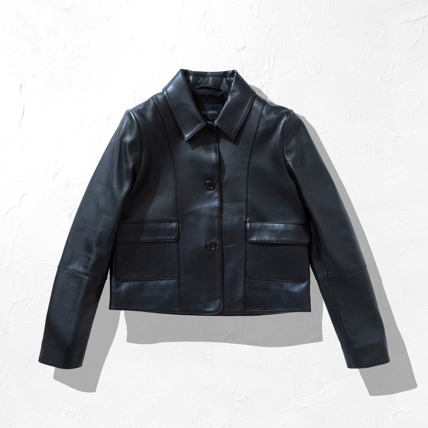 Black collared button leather jacket on a textured white background
