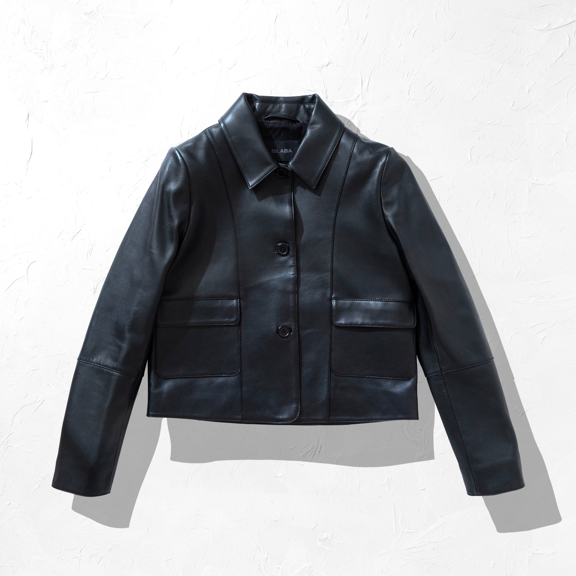 Black collared button leather jacket on a textured white background