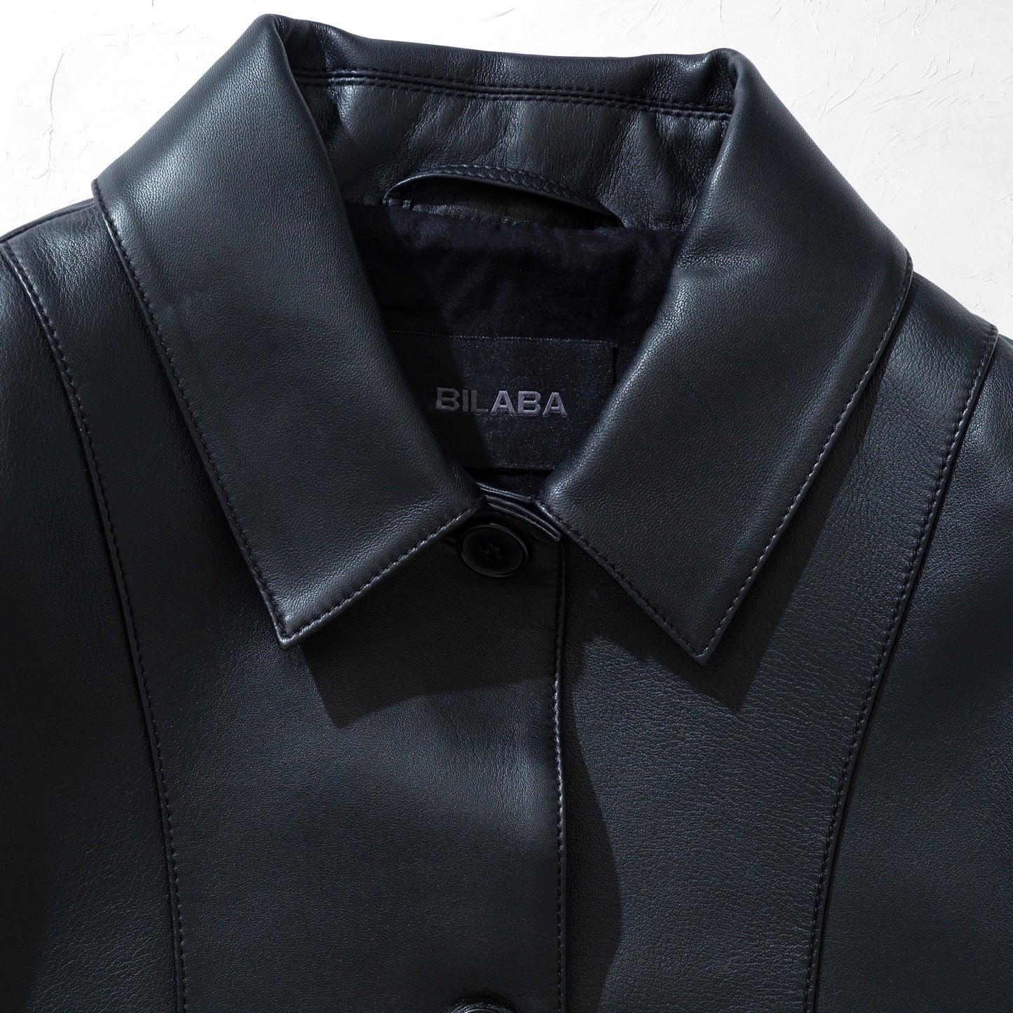 Close-up of a black leather jacket with a visible brand label on a white background