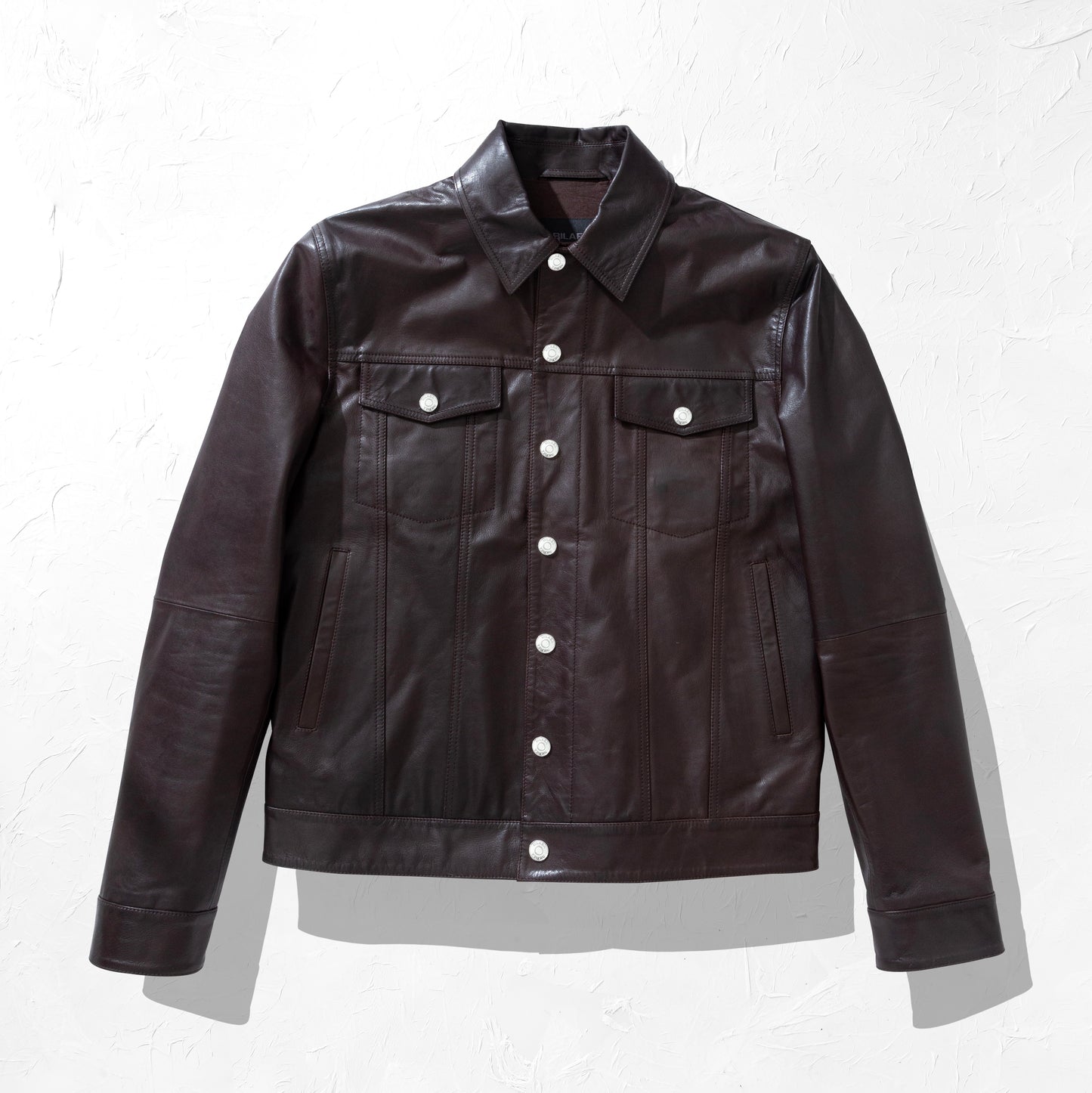 Dark brown leather jacket with white buttons on a light gray background