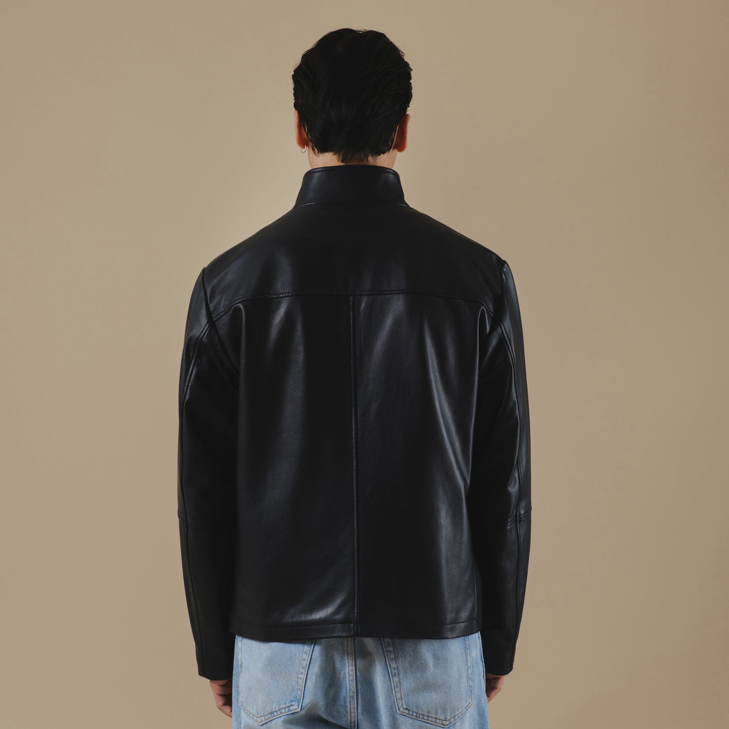 Person wearing a black leather jacket on a beige background