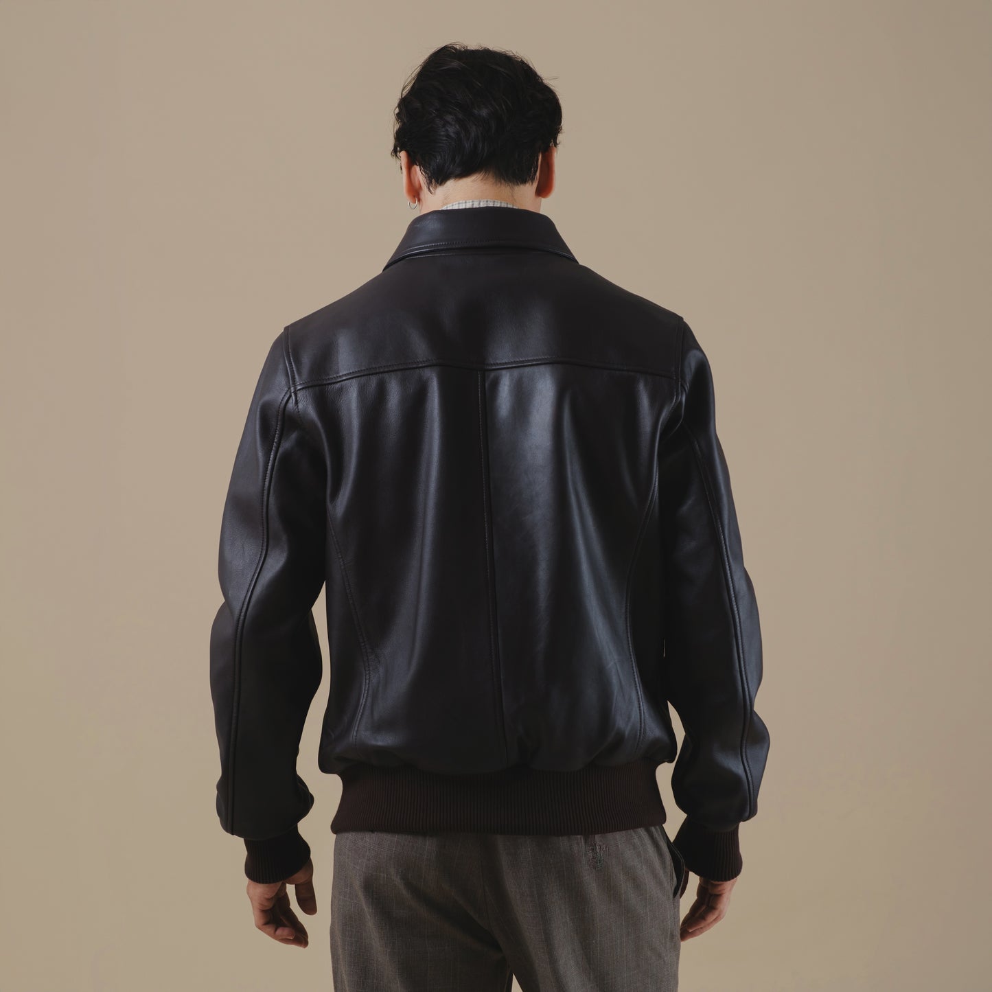 Man wearing a brown bomber leather jacket on a beige background