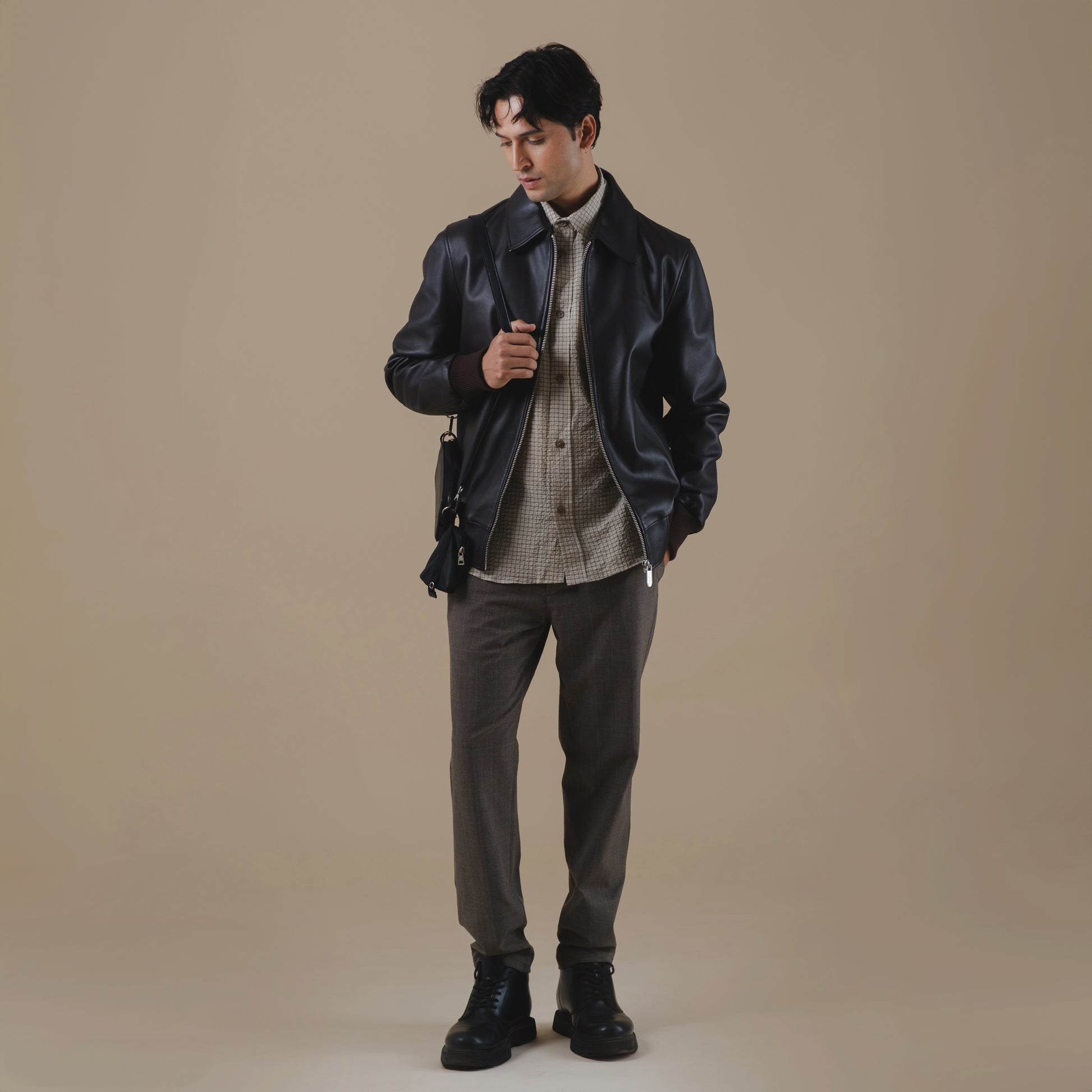 Man wearing a brown leather jacket and dark pants against a beige background