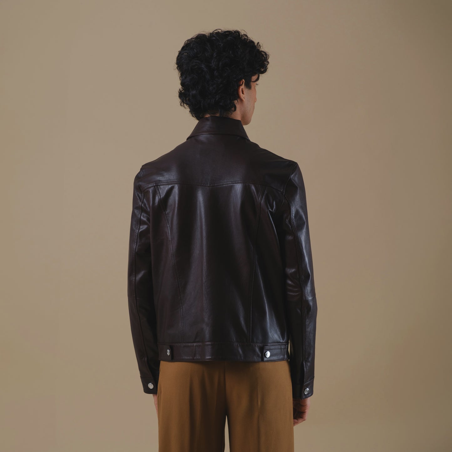 Man wearing a dark brown trucker leather jacket on a beige background