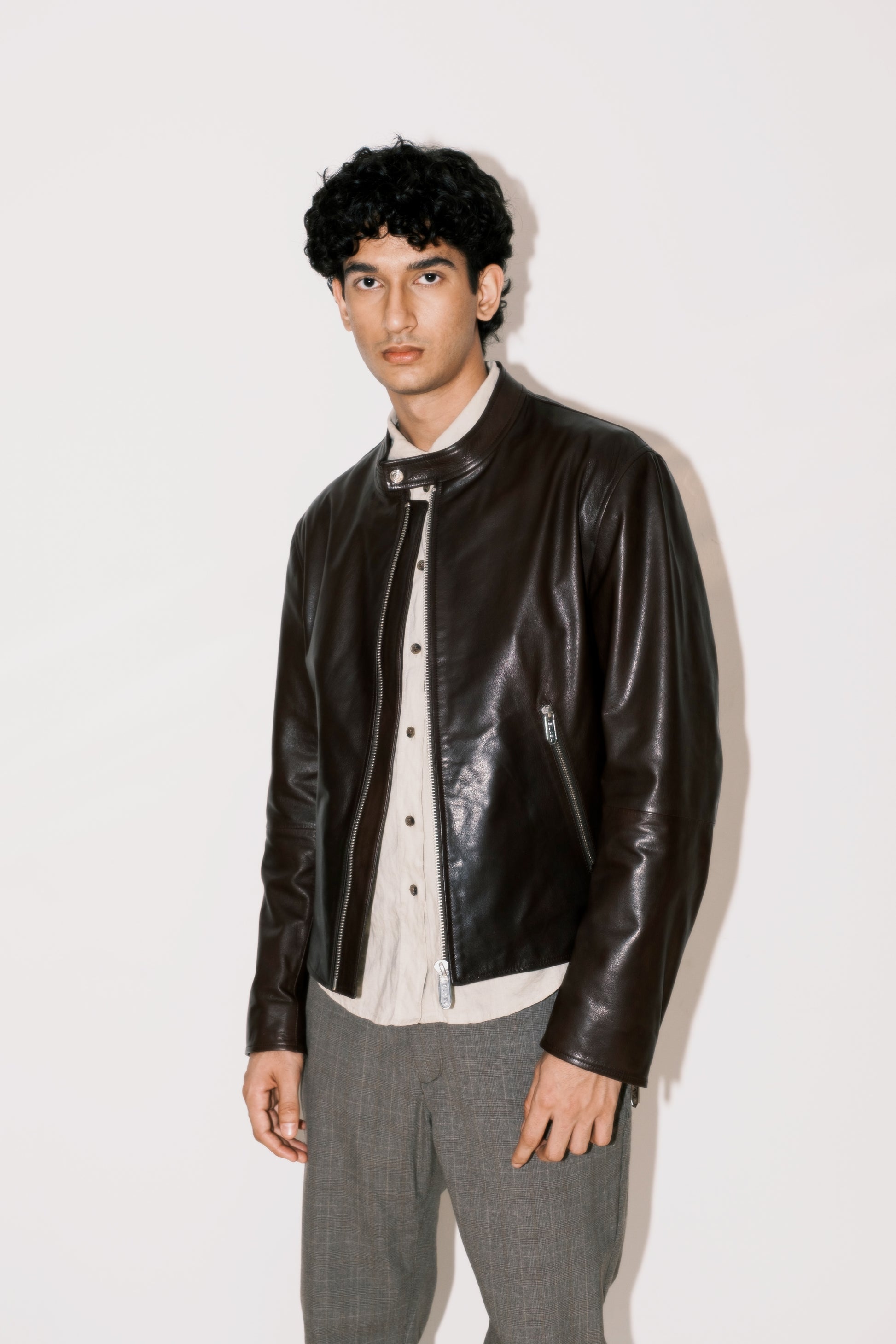 Man wearing a brown leather jacket over a white shirt with gray pants on a white background