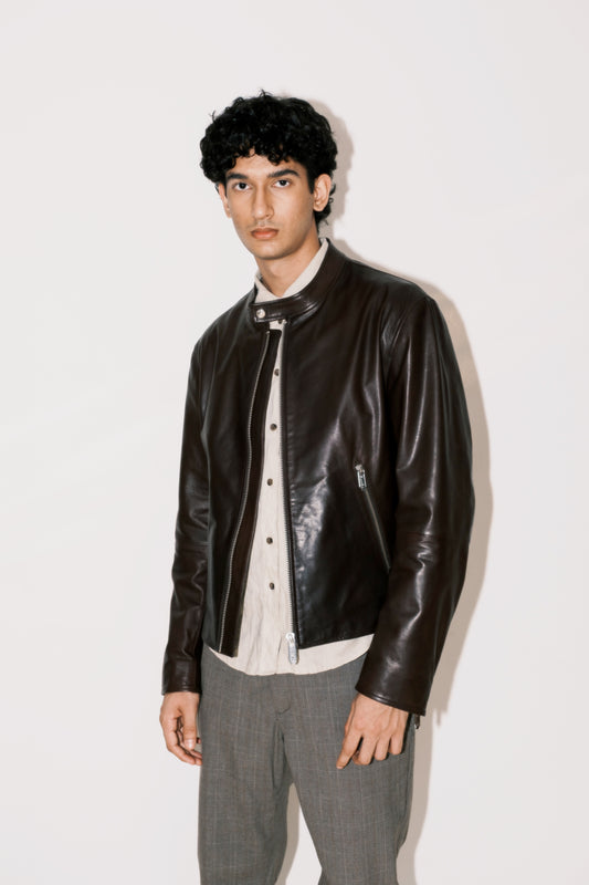 Man wearing a brown leather jacket over a white shirt with gray pants on a white background