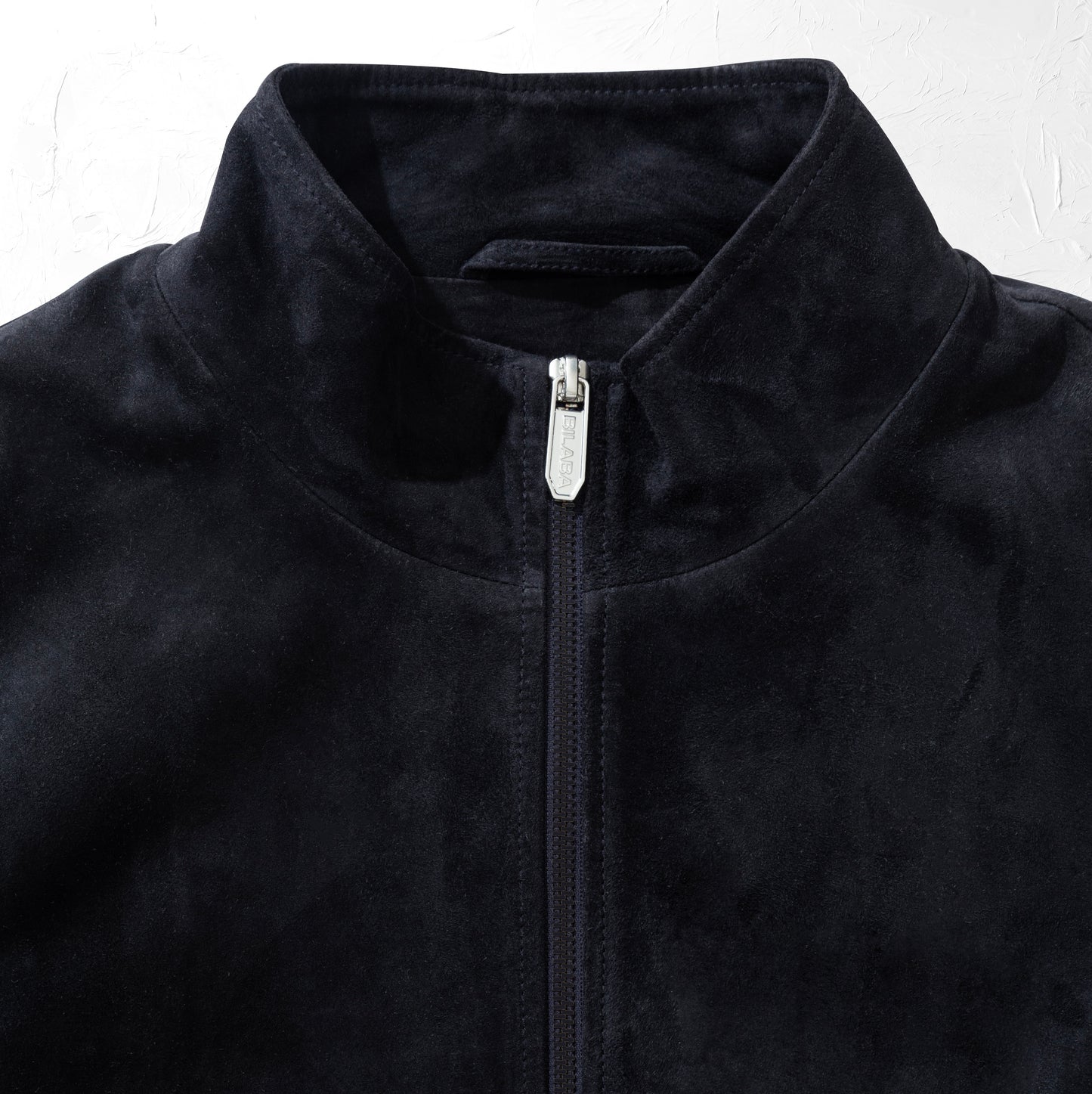 Close-up of a dark navy suede jacket with a zipper on a white background