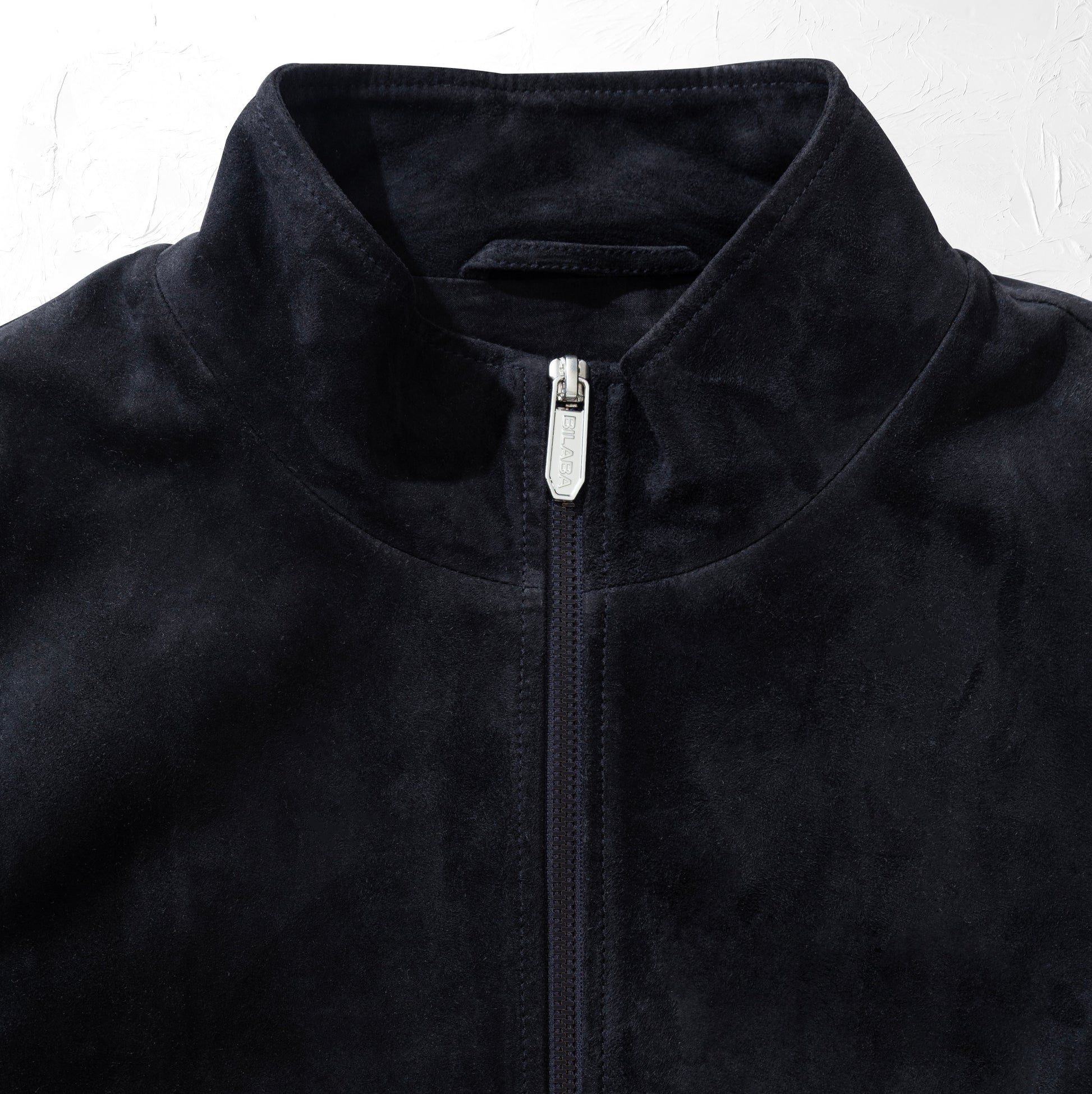 Close-up of a dark navy suede jacket with a zipper on a white background