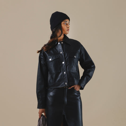 Person wearing a black trucker leather jacket and hat against a beige background