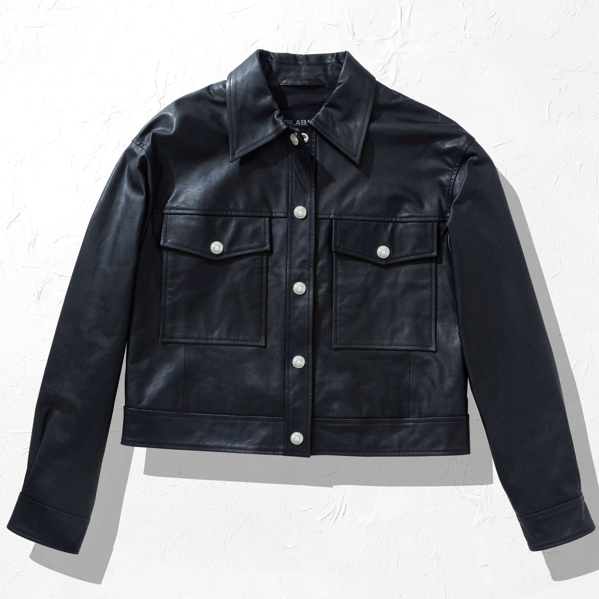 Black trucker leather jacket with white buttons on a light gray background